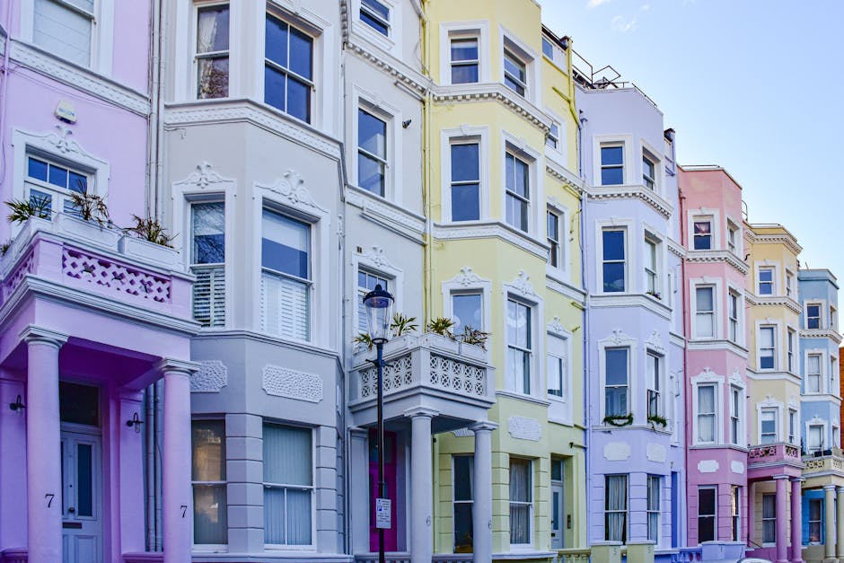 A row of multi-story residential buildings painted in pastel shades of purple, yellow, white, and pink, featuring detailed architectural elements such as decorative moldings, bay windows, and balconie